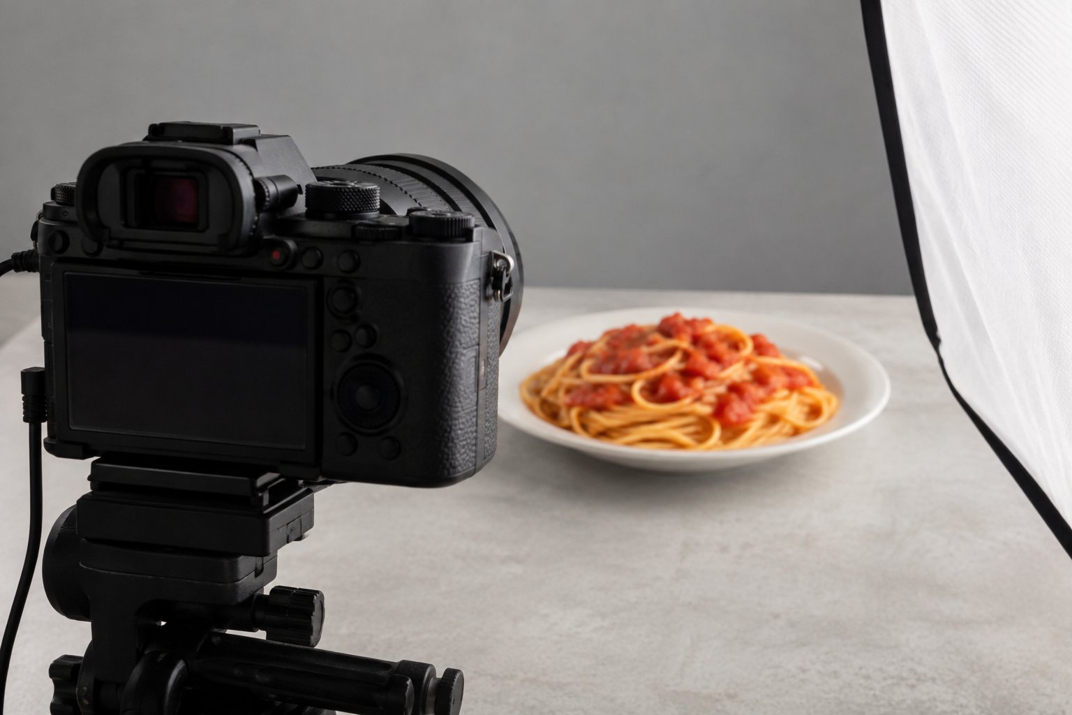 Cámara en tripié frente a un plato de pasta con salsa de tomate en un set iluminado