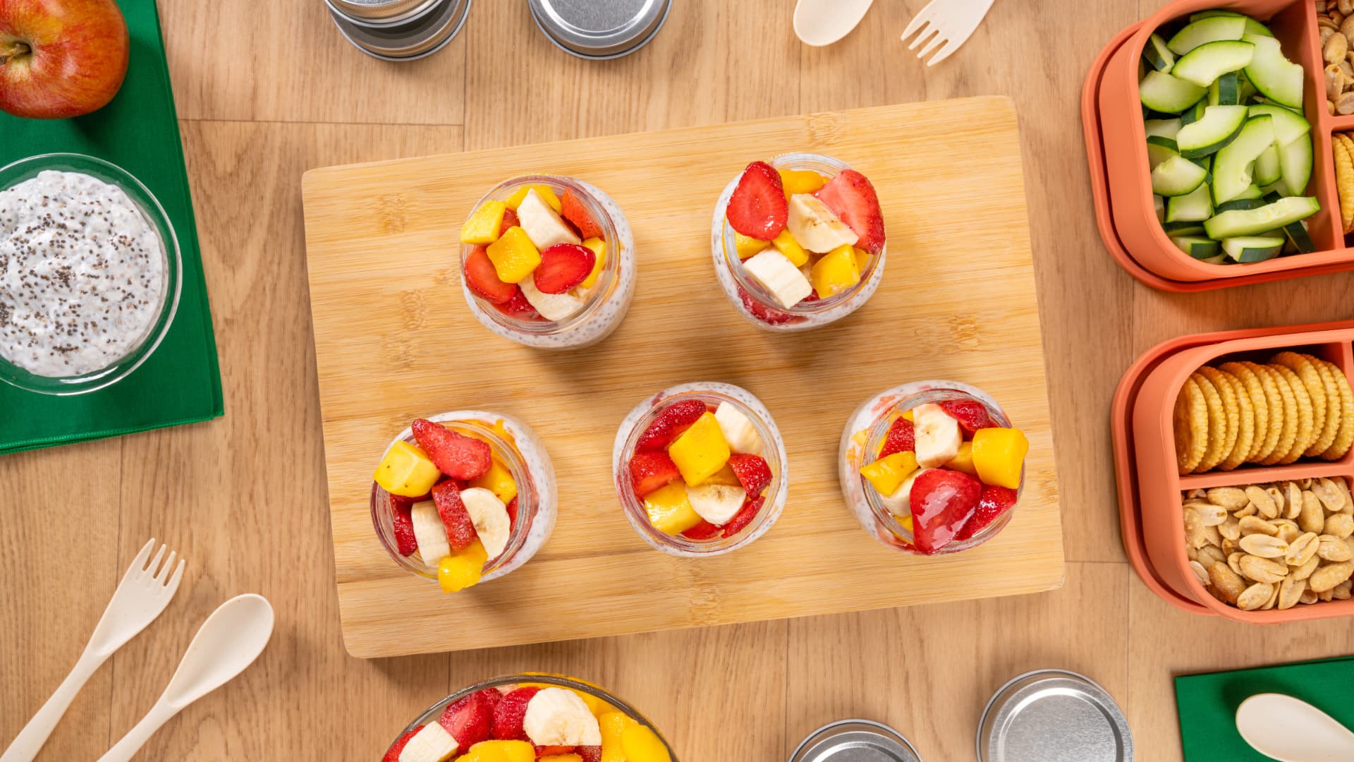 Mezcla tropical de chia pudding con fresa, mango y plátano en frascos de vidrio sobre tabla de bambú, vista cenital