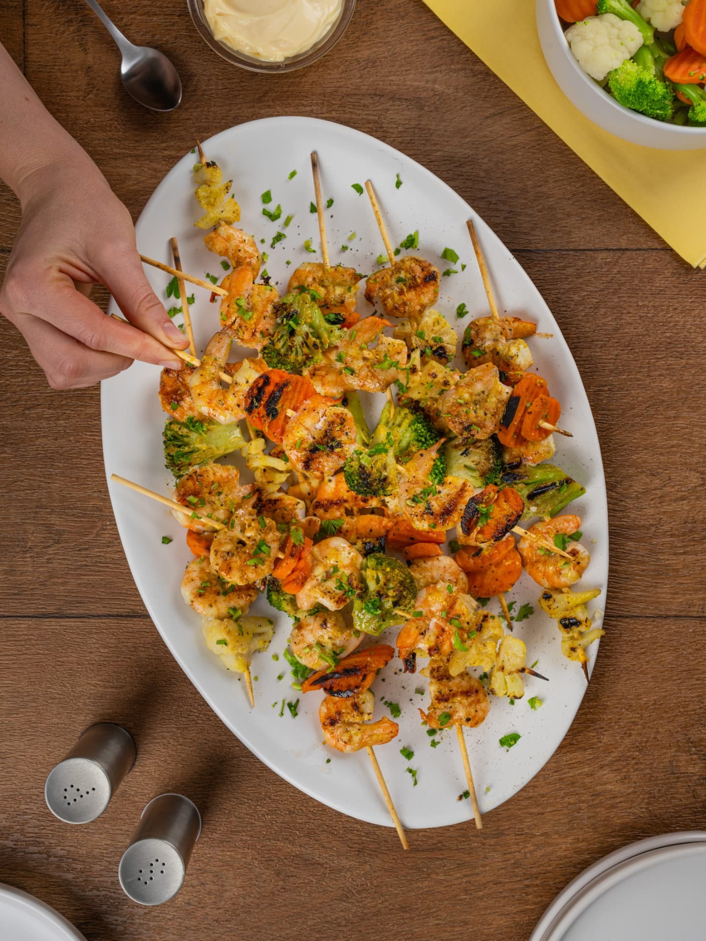 Brochetas de camarón con vegetales sobre plato blanco y mesa de madera