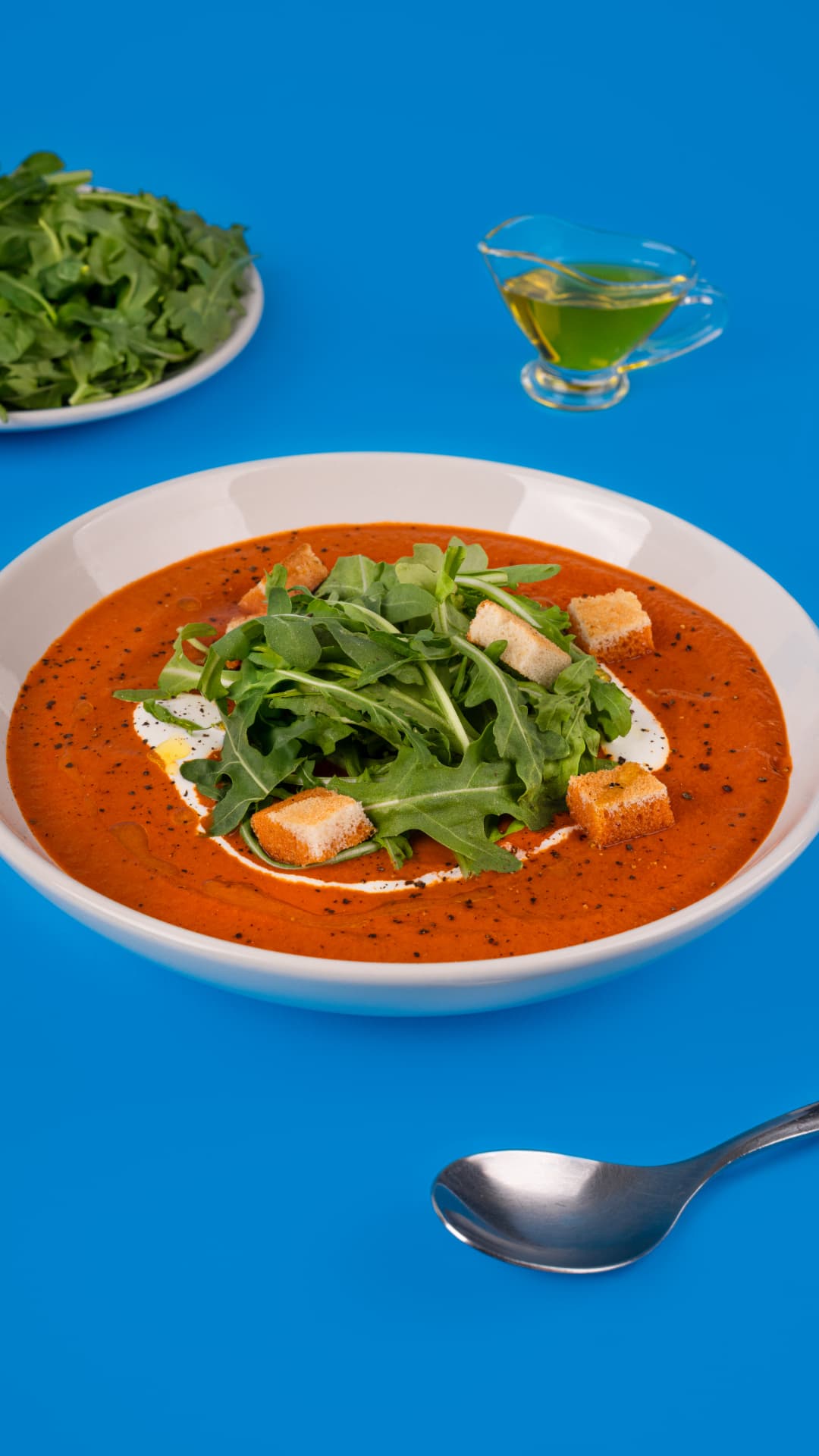Crema de tomate con arúgula, crutones y aceite de oliva sobre fondo azul