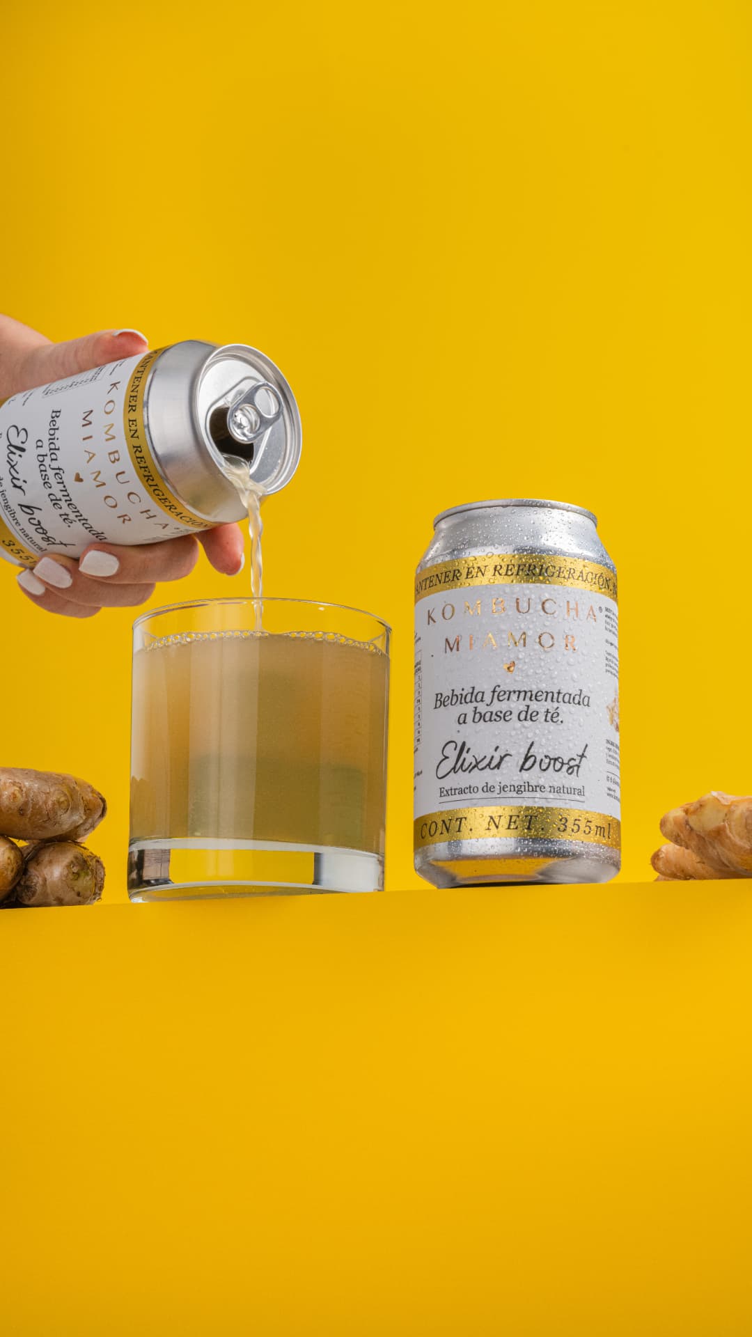 Lata de kombucha Elixir boost de jengibre sirviéndose en vaso sobre fondo amarillo