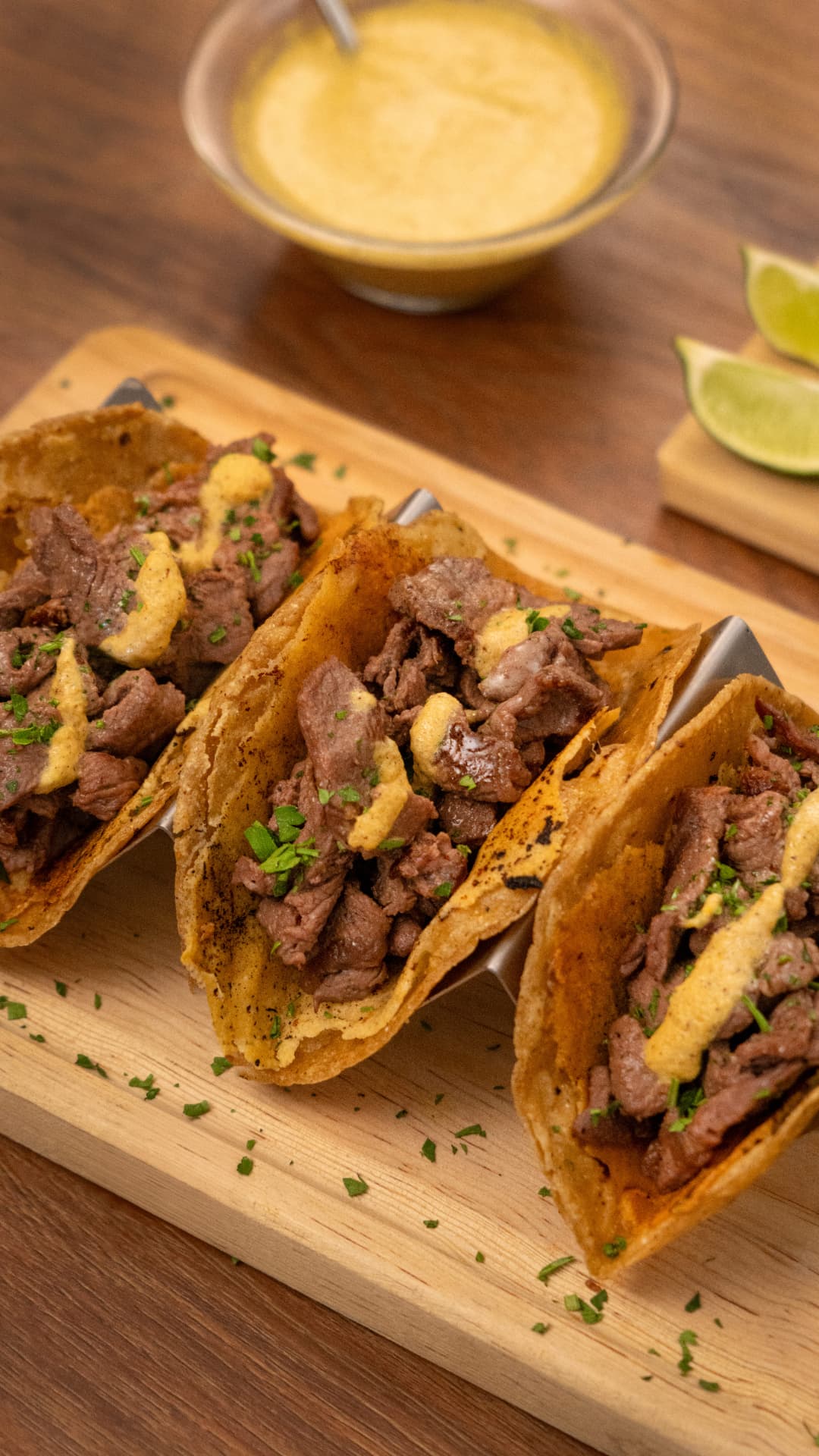 Tacos de sirloin con crema amarilla y hierbas picadas en soporte de metal sobre tabla de madera